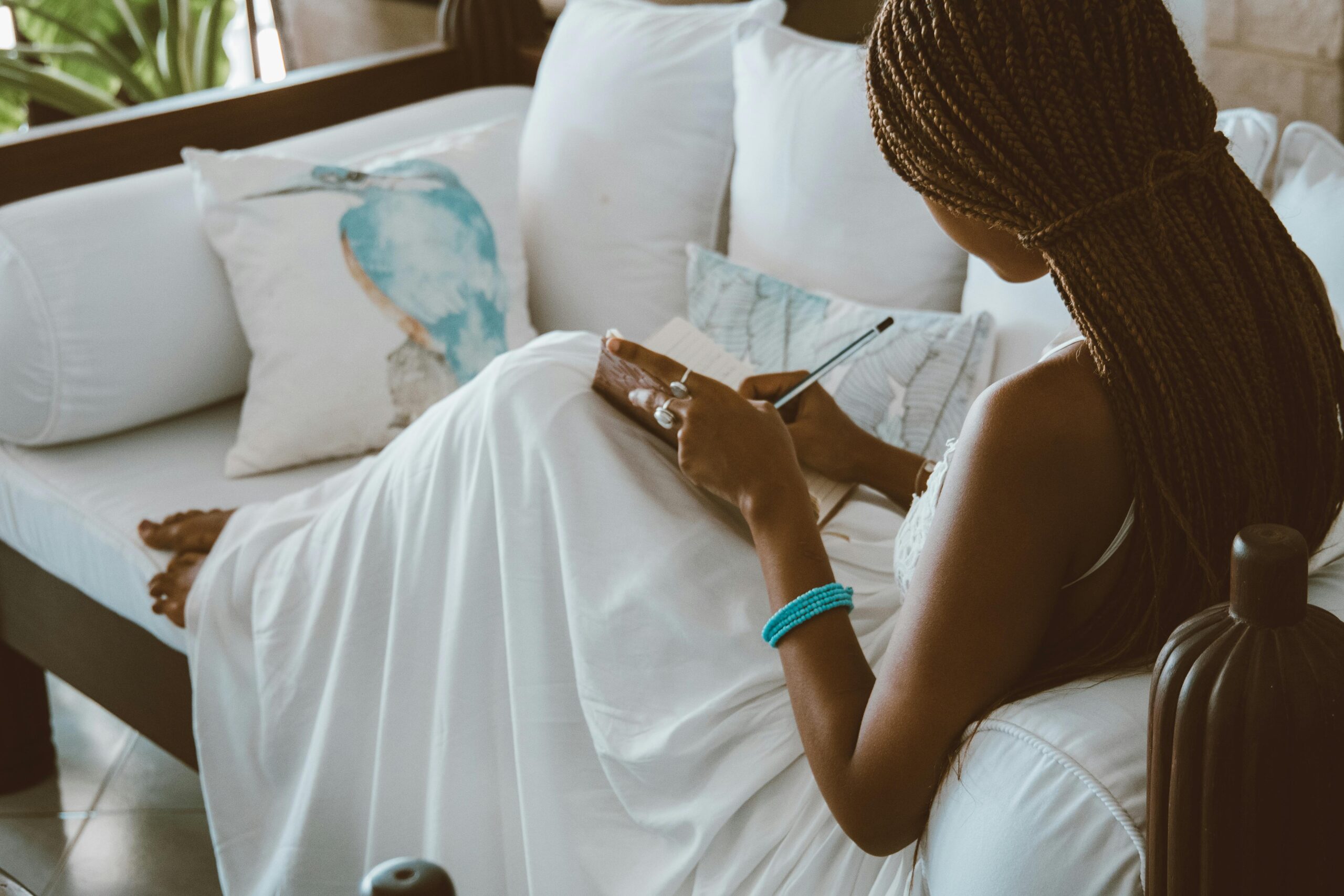 Woman in white sundress sitting on couch journaling